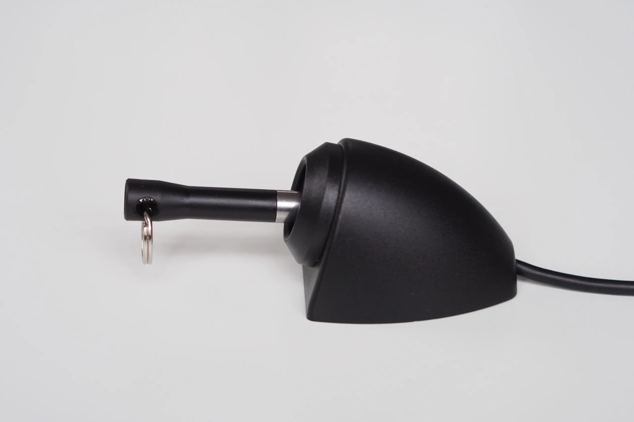 Nahaufnahme einer schwarzen Auto-Haifischflossenantenne mit einem Schlüsselring, der an einem davon ausgehenden schwarzen Zylinder befestigt ist, vor einem schlichten weißen Hintergrund.